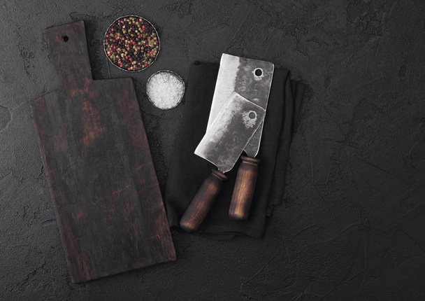 Vintage meat knife hatchets with vintage chopping board and black stone table background. Butcher utensils. Salt and pepper.  - Foto, Imagen