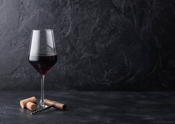 Elegant glass of red wine with corks and corkscrew on black stone background. Natural Light - Foto, afbeelding