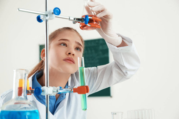 Smart pupil looking at flask with reagent on holder in chemistry class - Fotoğraf, Görsel