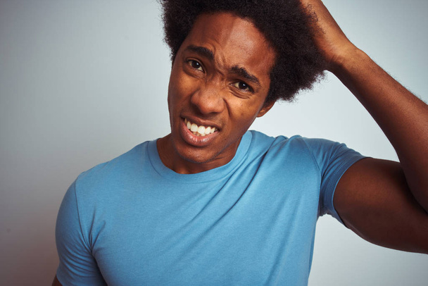 Afrikanisch-amerikanischer Mann mit Afro-Haaren in blauem T-Shirt vor isoliertem weißem Hintergrund, gestresst mit Hand auf Kopf, schockiert vor Scham und Überraschung, wütend und frustriert. Angst und Verärgerung wegen Fehlern. - Foto, Bild