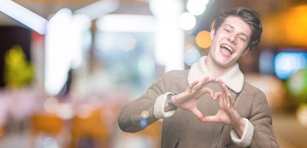 Young handsome man wearing winter coat over isolated background smiling in love showing heart symbol and shape with hands. Romantic concept. - Φωτογραφία, εικόνα