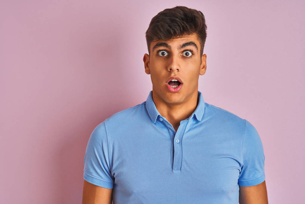 Jonge Indiase man het dragen van blauwe Polo staande over geïsoleerde roze achtergrond bang en geschokt met verrassing uitdrukking, angst en opgewonden gezicht. - Foto, afbeelding