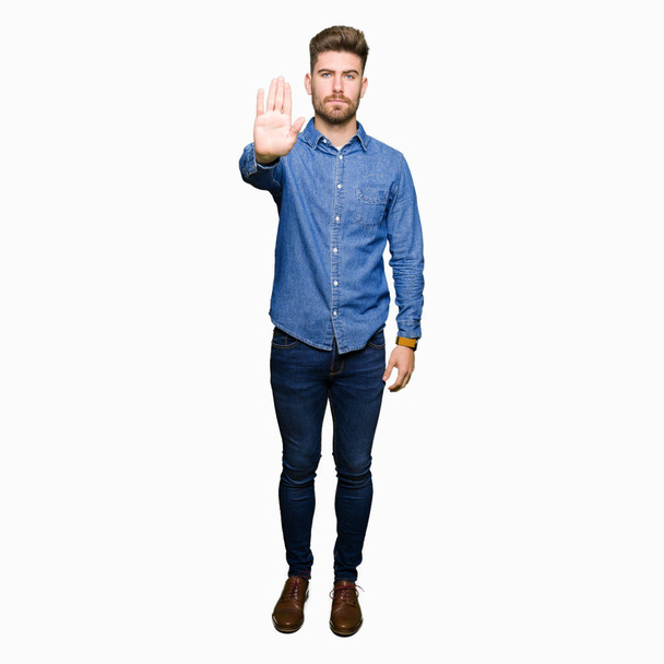 Young handsome blond man wearing casual denim shirt doing stop sing with palm of the hand. Warning expression with negative and serious gesture on the face. - Photo, Image