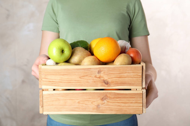Woman holding wooden crate with fruits and vegetables on color background, closeup - Фото, зображення