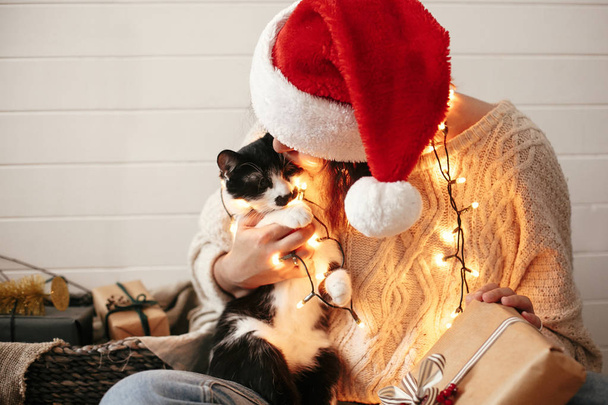Stylish happy girl in santa hat kissing and playing with cute ca - Photo, Image