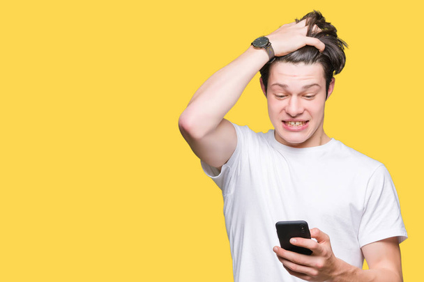 Jonge man met smartphone via geïsoleerde achtergrond benadrukt met de hand op het hoofd, geschokt met schaamte en verrassing gezicht, boos en gefrustreerd. Angst en boos voor fout. - Foto, afbeelding