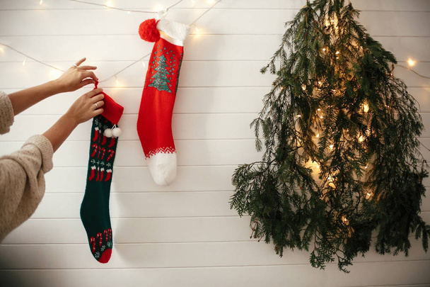 Κομψό κορίτσι σε άνετο πουλόβερ κρέμονται Χριστουγεννιάτικες κάλτσες, διακόσμηση - Φωτογραφία, εικόνα