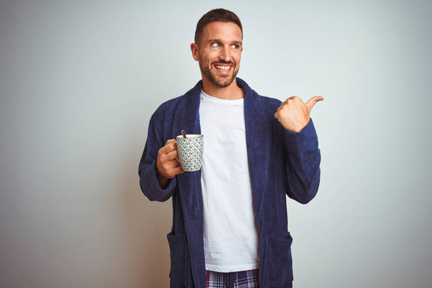 Mies yllään mukava pyjama ja kaapu juominen kuppi kahvia yli eristetty tausta vihainen kasvot, negatiivinen merkki osoittaa pidä peukalot alas, hylkääminen käsite
 - Valokuva, kuva