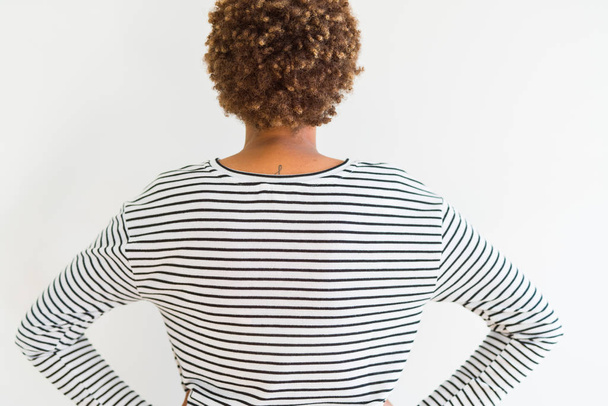 Genç güzel Afrikalı Amerikan kadın beyaz arka plan üzerinde çizgili kazak giyen geriye vücut üzerinde kollar ile bakıyor ayakta - Fotoğraf, Görsel