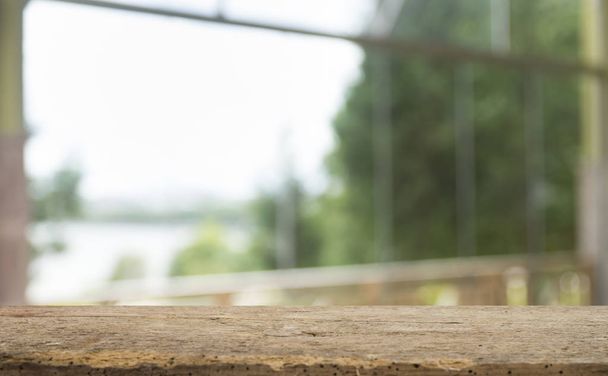 Üres a fa asztal tetejének elhomályosítja a függöny ablak kilátás zöld fa kert háttere. A montázs termék megjelenítéshez vagy design billentyűkiosztásra - Fotó, kép