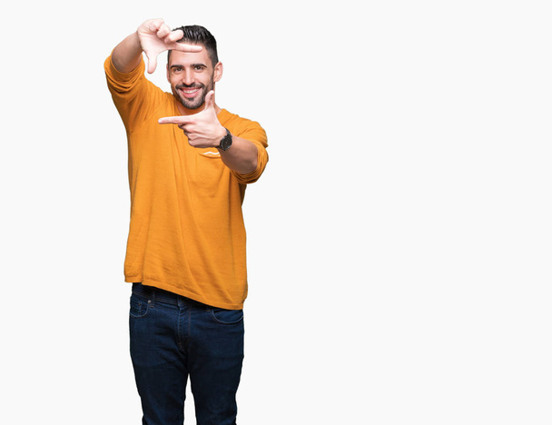Mladý pohledný muž izolované pozadí provedení rámu s rukama a prsty s šťastné tváře. Koncept kreativity a Fotografie. - Fotografie, Obrázek
