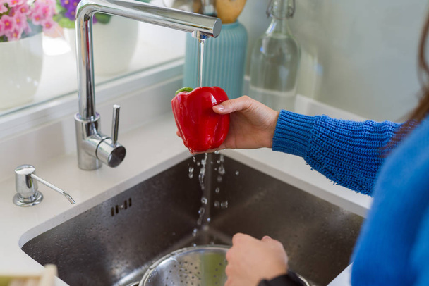 Fiatal nő mosás zöldségek és gyümölcsök vízzel a mosogató - Fotó, kép