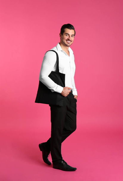 Young handsome man holding black tote bag on pink background, space for text - Photo, image