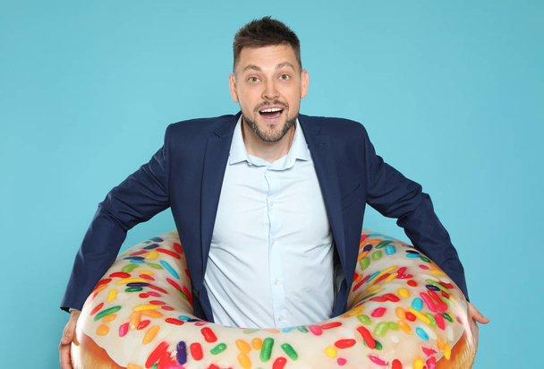 Funny businessman with bright inflatable ring on blue background - Zdjęcie, obraz