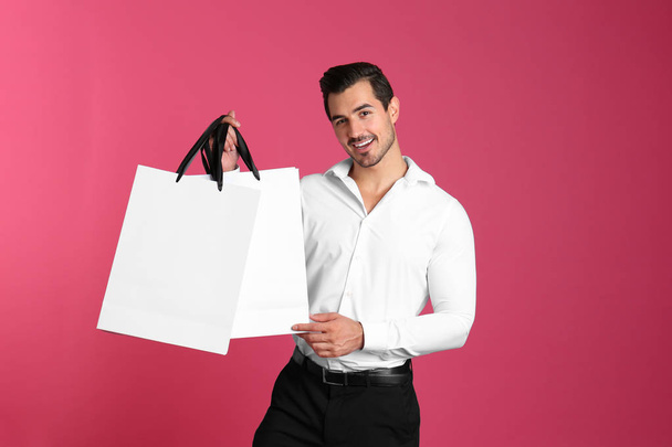 Young handsome man holding white paper bags on pink background. Mockup for design - Foto, afbeelding