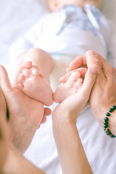 Children's feet in hands of mother and father. Mother, father and Child. Happy Family concept. Beautiful conceptual image of Motherhood - 写真・画像