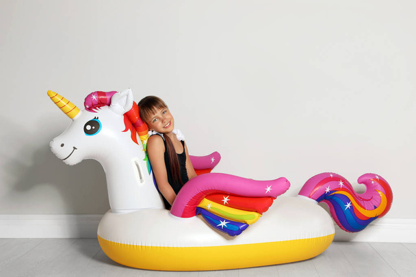 Cute little girl on bright inflatable ring near light wall - Foto, imagen