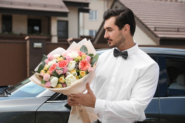 junger schöner Mann mit schönem Blumenstrauß in der Nähe von Auto im Freien - Foto, Bild