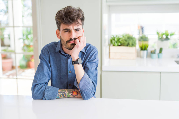 Young man wearing casual shirt sitting on white table thinking looking tired and bored with depression problems with crossed arms. - Photo, Image