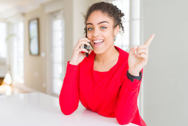 Nuori afrikkalainen amerikkalainen nainen, jolla on keskustelu puhuminen älypuhelimella erittäin onnellinen osoittaa käsin ja sormella sivulle
 - Valokuva, kuva