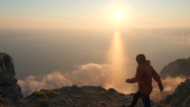 Silhuette Nuoren miehen aseita ojensi tarkkailemalla kaunis dramaattinen värikäs auringonlasku yläpuolella meren korkealta vuorelta Krimillä
. - Materiaali, video