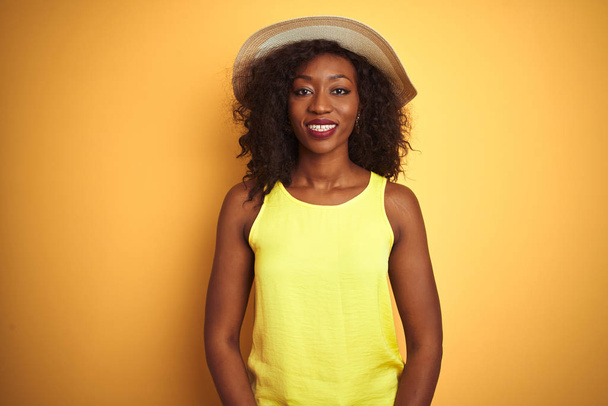 Jeune femme afro-américaine portant t-shirt et chapeau sur fond jaune isolé avec un sourire heureux et cool sur le visage. Personne chanceuse
. - Photo, image