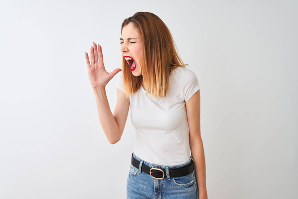 Bella rossa donna indossa casual t-shirt in piedi sopra isolato sfondo bianco urlando e urlando forte a lato con mano sulla bocca. Concetto di comunicazione
. - Foto, immagini