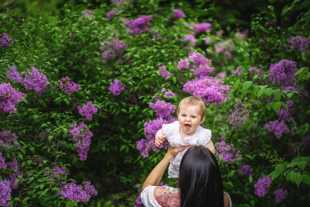 Authentic woman throwing her baby up into the sky, Happy family time in the park. Blooming trees all around - Foto, afbeelding