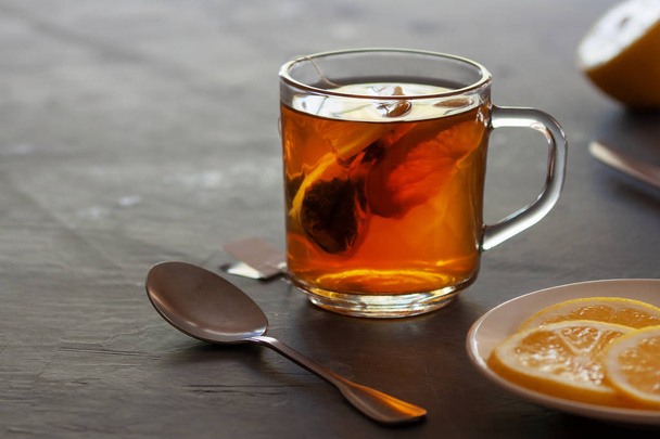 Cup of tea with tea bag and lemon slices on dark background - Фото, изображение