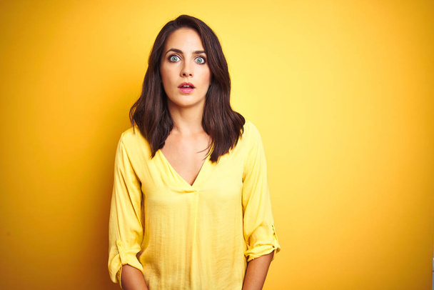 Beautiful elegant woman standing over yellow isolated background afraid and shocked with surprise expression, fear and excited face. - Фото, изображение