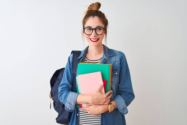 Redhead student woman wearing backpack holding books over isolated white background with a happy face standing and smiling with a confident smile showing teeth - Fotografie, Obrázek