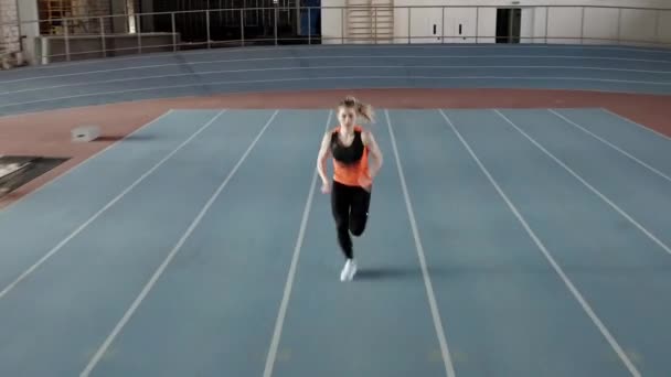 Sportive blonde woman running at indoor stadium - Materiaali, video
