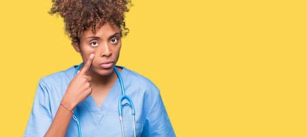 Молодий афроамериканець лікар жінка над ізольованих тло наведення на очі спостерігаючи ви жест, підозрілі вираз - Фото, зображення