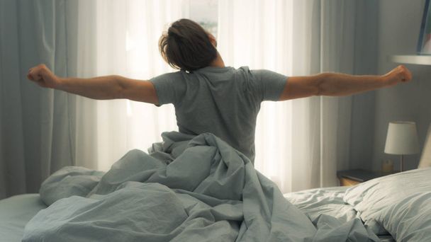Handsome Fair Boy Stretches Lazily in the Bed After Waking Up. Young and Fit Caucasian Man Greeting New Day. Early Morning Sun Shines Through the Window. - Photo, image