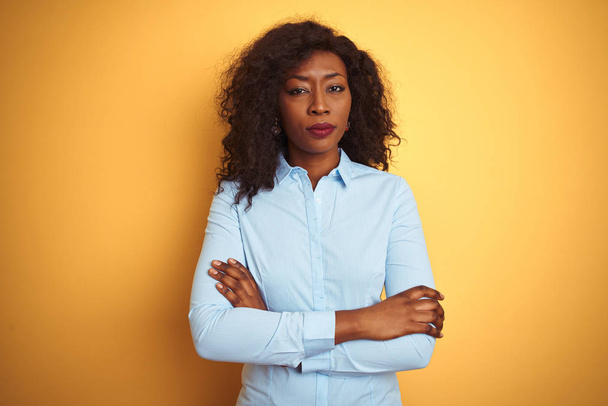 Африканская американская деловая женщина в элегантной рубашке на изолированном жёлтом фоне скептически и нервно, неодобрительное выражение лица со скрещенными руками. Отрицательное лицо
. - Фото, изображение