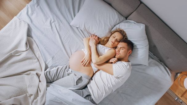 Happy Young Couple Sleeping Together in the Bed, Sweet Loving Young People Holding Each other while Sleeping. Beautiful Woman is Pregnant, Loving Partner Supports Her By Being there For Her. - Photo, Image