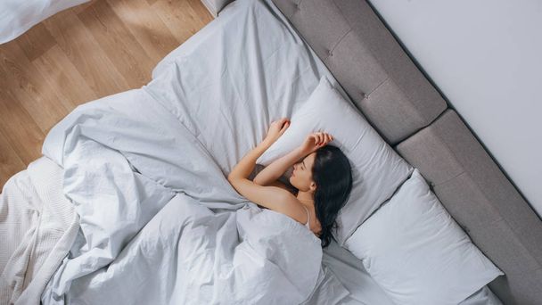 Привлекательная Брюнетка уютно спит в своей постели, в то время как ранним утром солнечные лучи освещают ее. Теплая, уютная и сладкая картина спящей красавицы
 - Фото, изображение