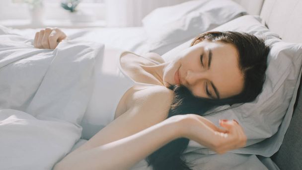 Attractive Brunette Cozily Sleeps in Her Bed while Early Morning Sunrays Illuminate Her. Warm, Cozy and Sweet Picture of Beauty Sleeping - Fotó, kép
