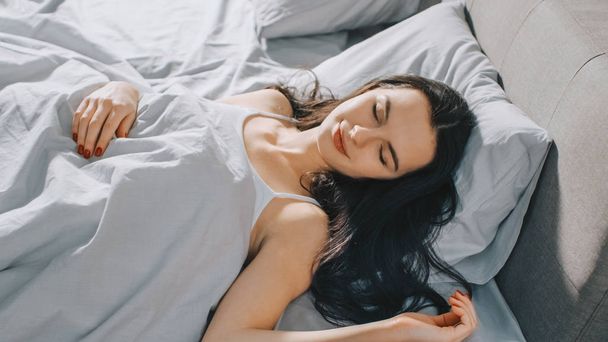 Attractive Brunette Cozily Sleeps in Her Bed while Early Morning Sunrays Illuminate Her. Warm, Cozy and Sweet Picture of Beauty Sleeping - Photo, image