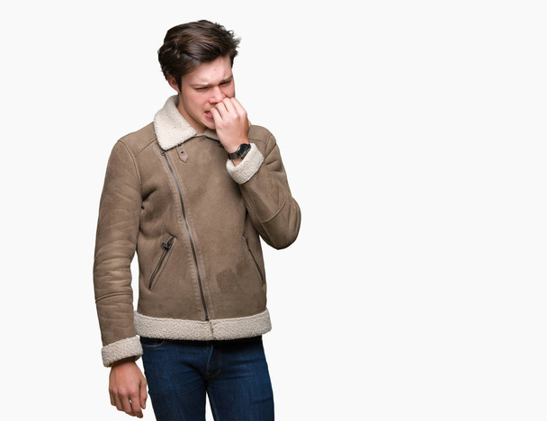 Young handsome man wearing winter coat over isolated background looking stressed and nervous with hands on mouth biting nails. Anxiety problem. - Foto, Imagen