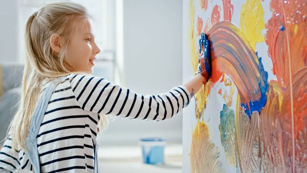 Happy Little Girl with Hands Dipped in Vivid Paint Draws Colorful Abstractions on the Wall. She is Having Fun and Laughs. Home is Being Renovated. - Zdjęcie, obraz