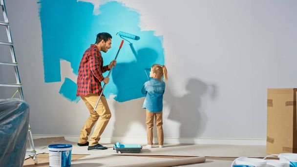 Young Father is Showing How to Paint Walls to Cute Small Daughter. They Paint Together with Rollers that are Covered in Light Blue Paint. Room Renovations at Home. - Φωτογραφία, εικόνα