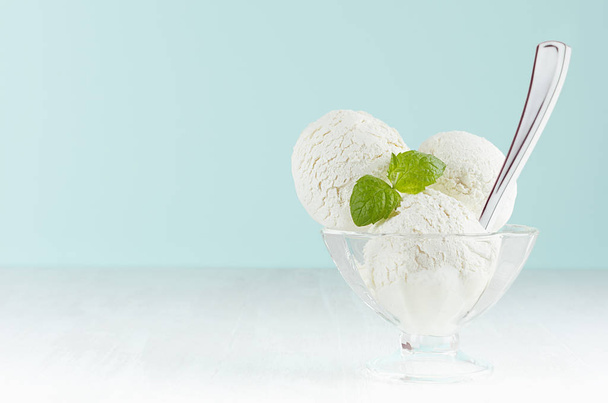 Homemade creamy ice cream scoops in transparent glass ice-cream bowl with green mint, silver spoon in modern blue interior on white wood board. - Foto, imagen