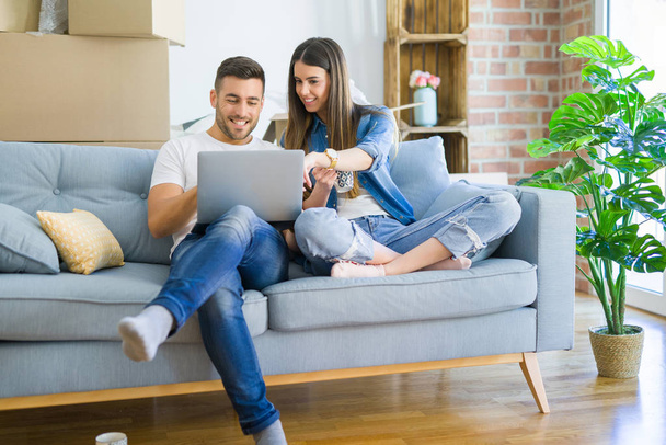 Młoda para porusza się do nowego domu relaksujący siedząc na kanapie za pomocą laptopa komputerowego, uśmiechnięty szczęśliwy do przejścia do nowego mieszkania - Zdjęcie, obraz
