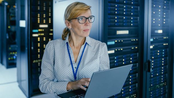 Staand shot in Data Center: vrouwelijke IT-technicus die het onderhoudsprogramma op een laptop uitvoert, regelt de operationele server rack optimaal functioneren. Hightech telecommunicatie operationeel Data Center - Foto, afbeelding