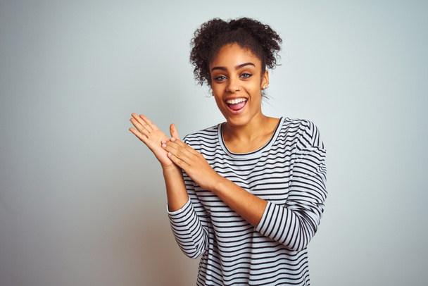 Africká Američanka nosí na sobě pruhovanou košili, která stojí nad osamělým bílým pozadím a tleská, radostně a vesele se usmívá hrdé ruce - Fotografie, Obrázek