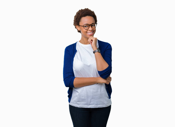 Jonge mooie Afrikaanse Amerikaanse vrouw bril over geïsoleerde achtergrond op zoek vertrouwen op de camera met glimlach met gekruiste armen en hand op kin aan de orde gesteld. Positief denken. - Foto, afbeelding