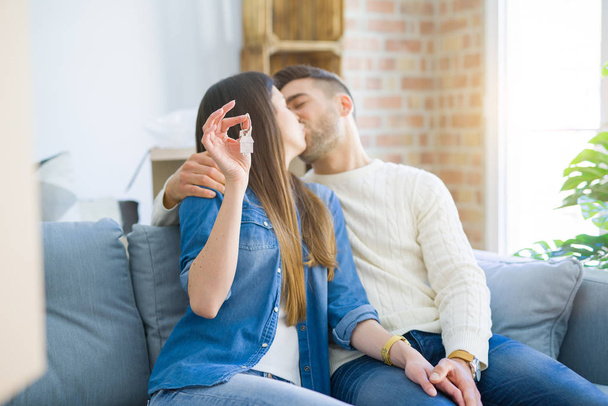Young couple moving to a new home, hugging in love showing keys of new apartment smiling very happy - Photo, Image