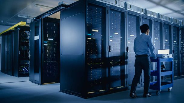 In the Modern Data Center: IT Engineer Doing Maintenance and Diagnostics. Pushes Cart alongside Server Racks. Planned System Equipment Update and Maintanence. - 写真・画像