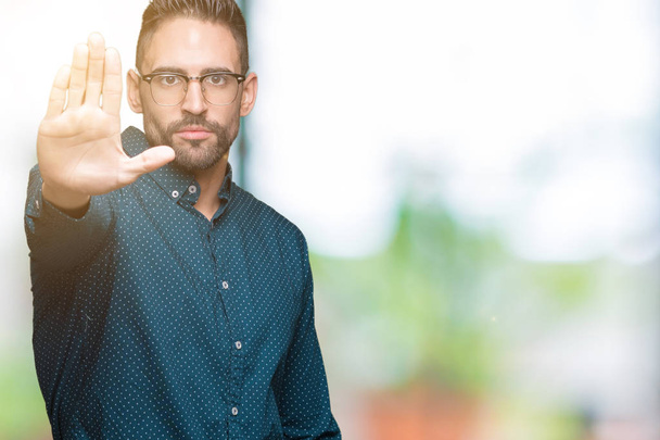 Young handsome business man wearing glasses over isolated background doing stop sing with palm of the hand. Warning expression with negative and serious gesture on the face. - Photo, Image